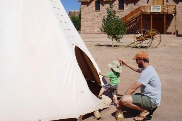 Father helping child to get into a teepee at Bluff Fort